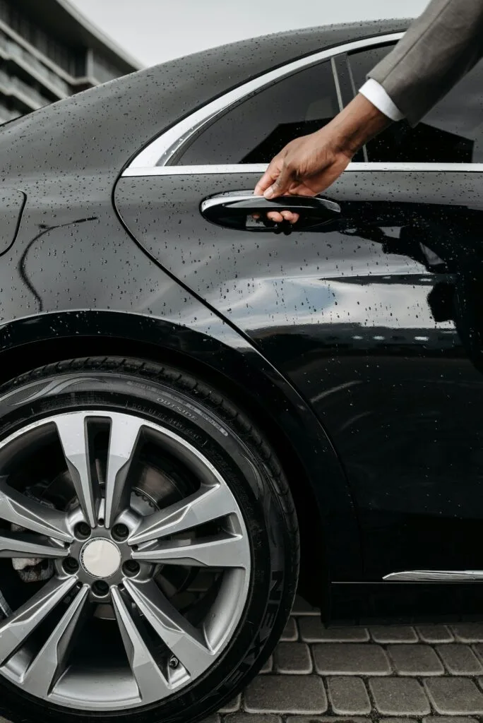 Close-up of a hand opening a black luxury car door on a rainy day. Elegant and modern design.